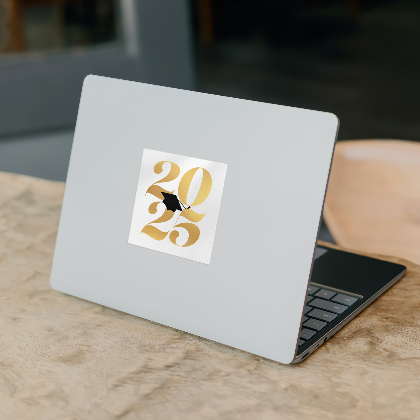 White square sticker with 2025 in gold and a black graduation cap placed in the middle stuck in the middle of a silver laptop on a desk.