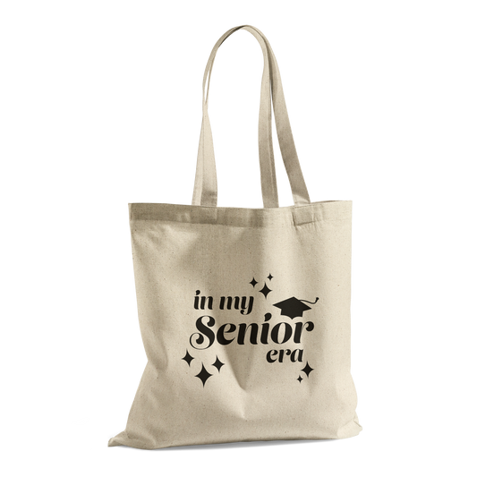 Tan canvas tote bag with the phrase “In My Senior Era” and a graduation cap printed in black ink.