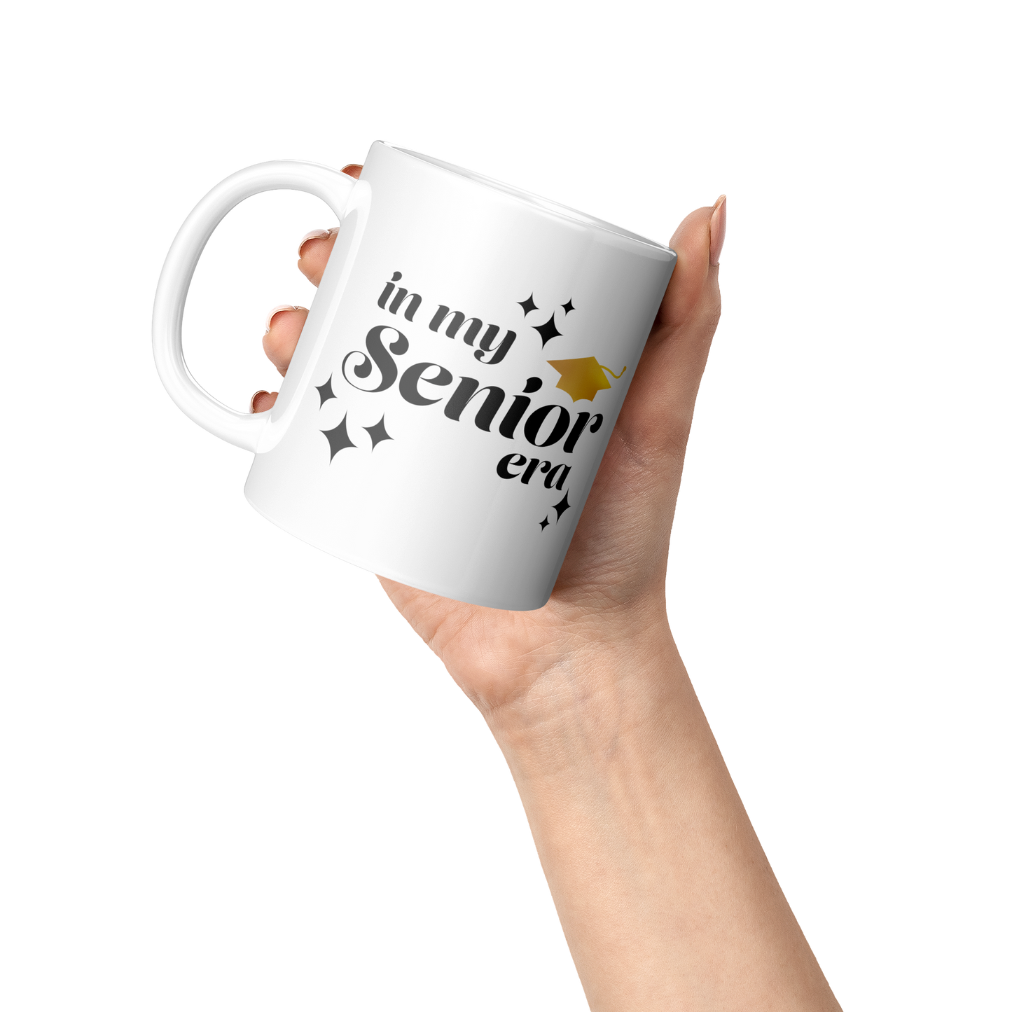 11oz white mug with the phrase “In My Senior Era” in black ink and a gold graduation cap being held by one hand at an angle.