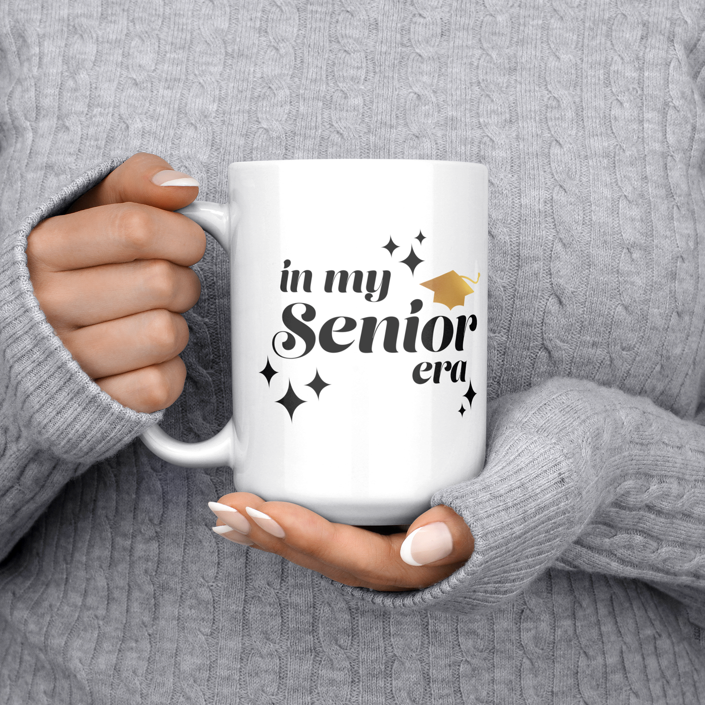 15oz white mug with the text "In My Senior Era" in black and a gold graduation cap being held by two hands.