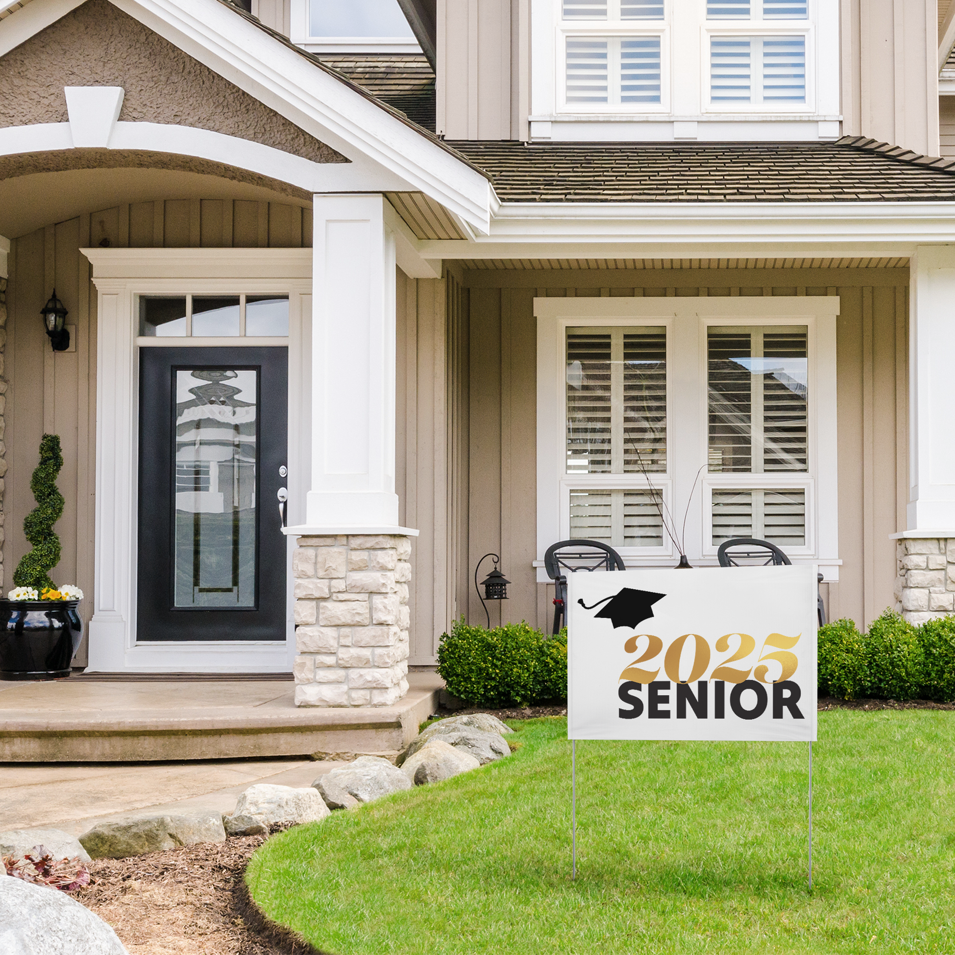 White vinyl yard sign with 2025 in gold, Senior in black text, and a black graduation cap in the top left placed in the yard of a two story house. 