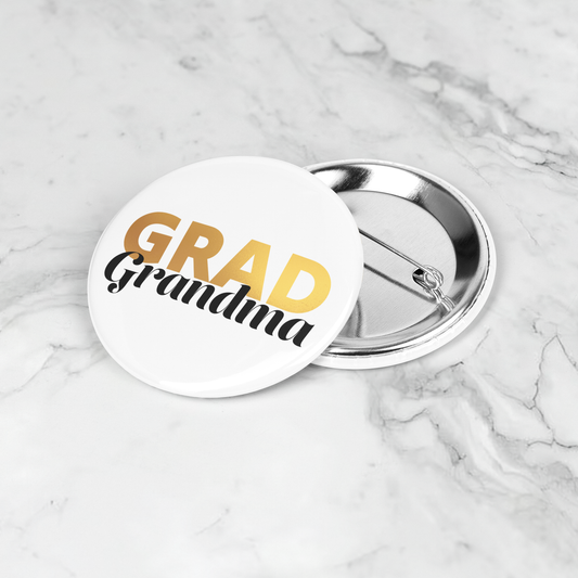 White button pin with Grad in gold and grandma in black, laying on a marble surface.