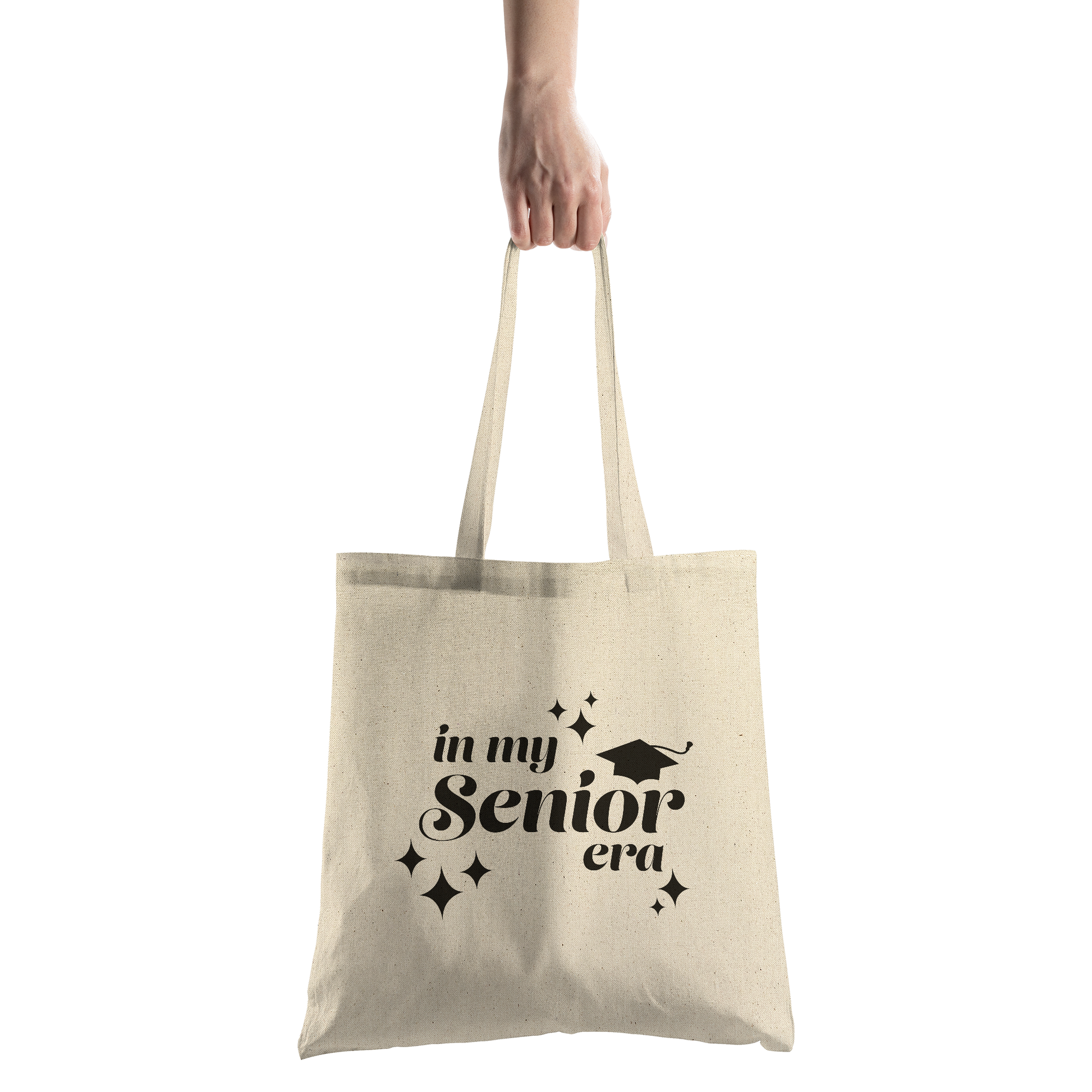 Tan canvas tote bag with the phrase “In My Senior Era” and a graduation cap printed in black ink being held by a hand