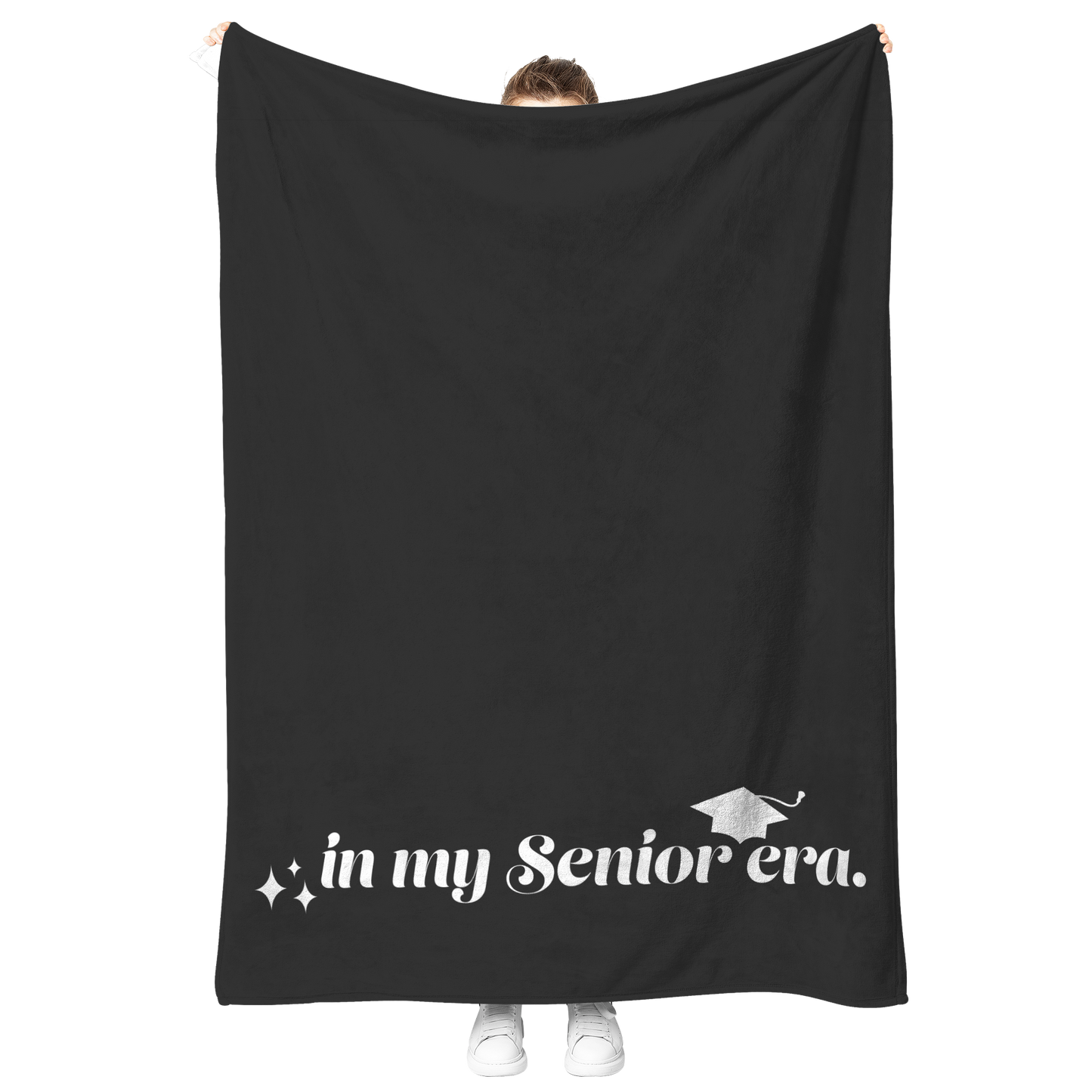 A black fleece blanket with the phrase "In My Senior Era" and a graduation cap in white at the bottom being held up.