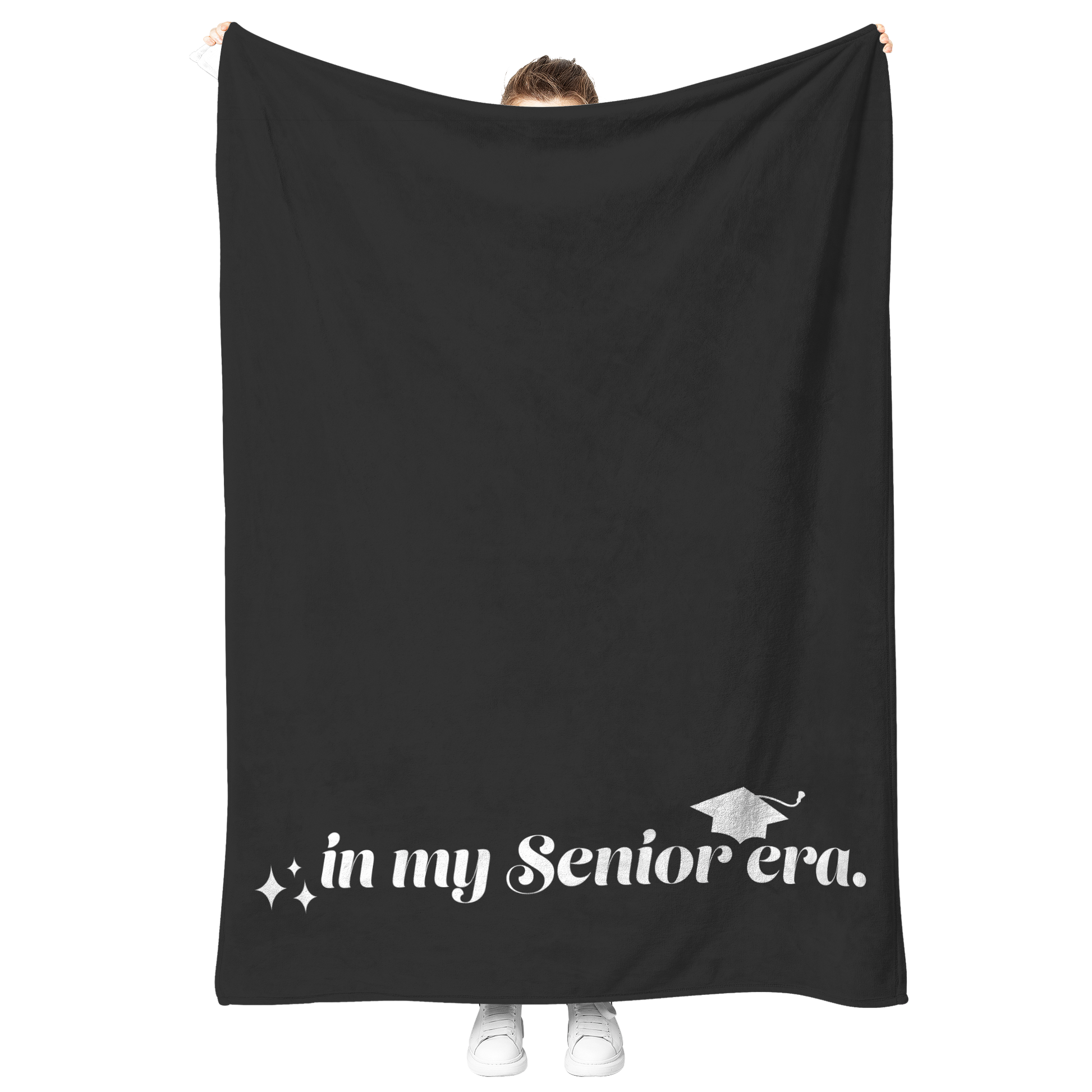 A black fleece blanket with the phrase "In My Senior Era" and a graduation cap in white at the bottom being held up.