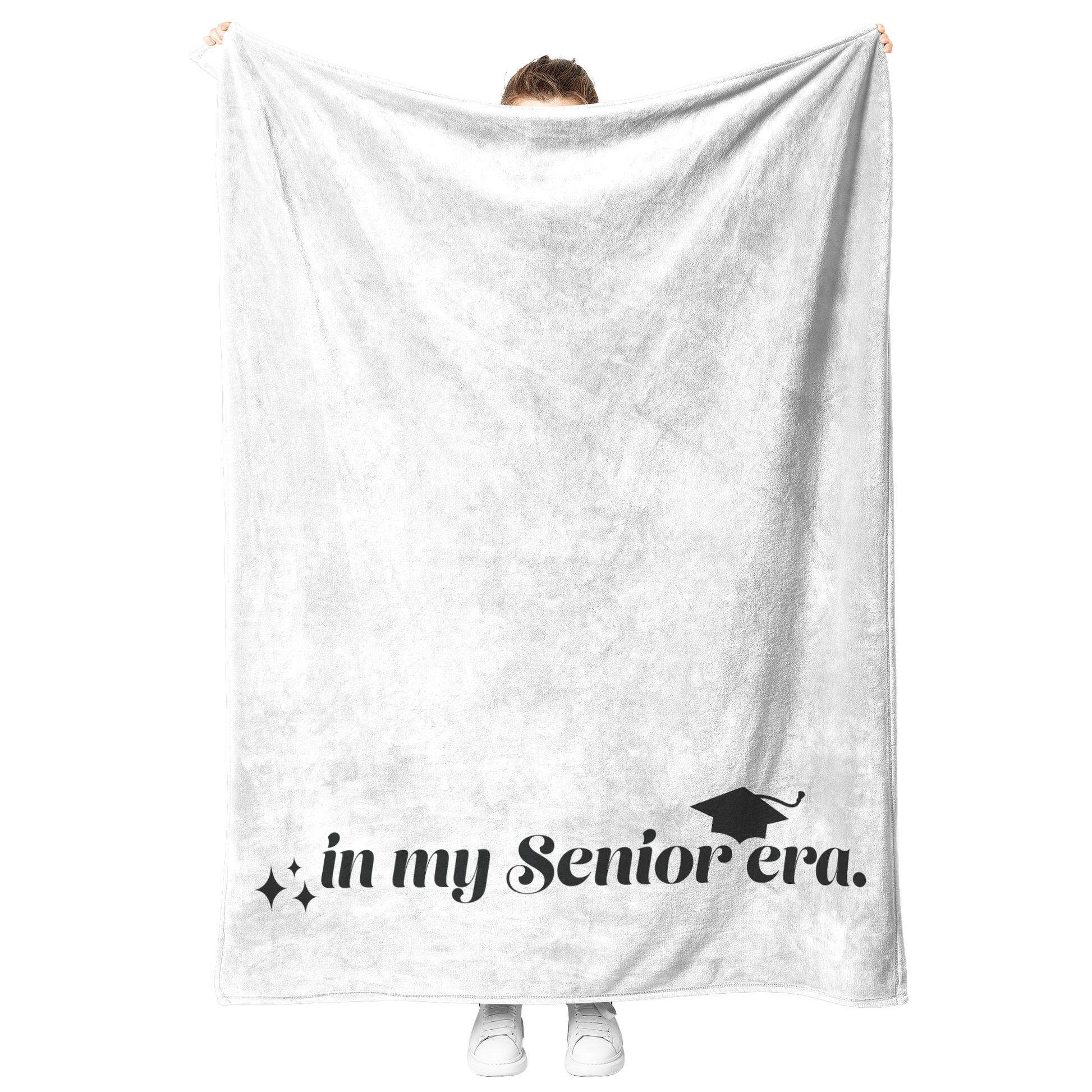 A white fleece blanket with the phrase "In My Senior Era" and a graduation cap in black at the bottom being held up.