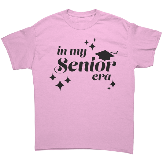 Light pink t-shirt with the phrase “In My Senior Era” printed on the front in black ink, along with a black graduation cap and stars. 